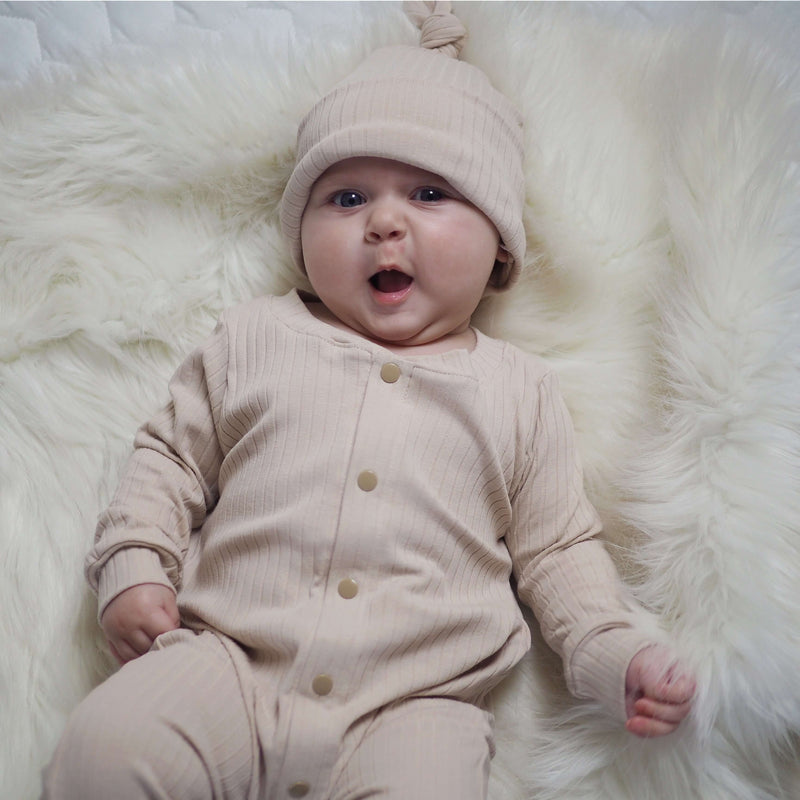 baby girl wearing a beige ribbed babygrow with matching knotted baby hat