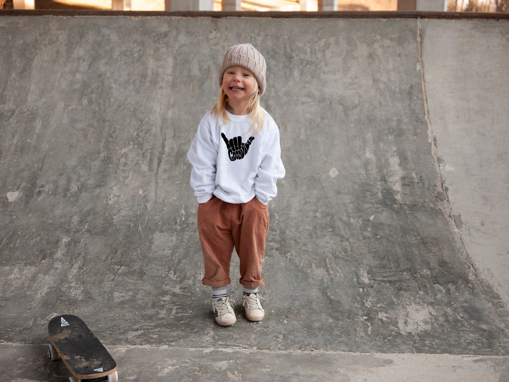 Trendy toddler clothes by Lottie & Lysh. Good vibes shacka sweatshirt in white worn by a little boy standing on a skate ramp