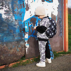 Boy wearing an animal print tracksuit, beige knitted hat and black backpack with white madala lion design