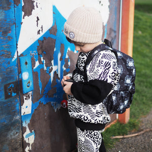 Young boy wearing a Lottie & Lysh Safari print mashup tracksuit, beige beanie hat with smile face and Lion Noir toddler backpack