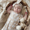 sleeping baby girl wearing a beige romper with white daisy detail with matching bow headband