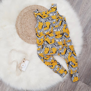 Flat lay featuring Lottie & Lysh mustard zebra toddler dungarees. The fabric is mustard yellow, with zebra print detail. The Dungarees are photographed against a white sheepskin rug and there is a wooden toy camera alongside.