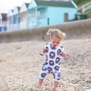 Toddler girl wearing Lottie & Lysh Aztec Lion organic romper on the beach with beach huts in the distance