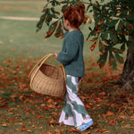 Lottie & Lysh berry burst flares worn by a toddler girl with red hair. Paired with a green knitted sweatshirt. The girl is pick leaves from a tree, and there are many autumnal coloured leaves on the ground