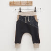 Lottie and Lysh Harem slouch jogging bottoms for children and babies. The trousers are black and beige, with printed splatter accents in black in white. They are photographed hanging on a wooden hanging rail against a white wall. 
