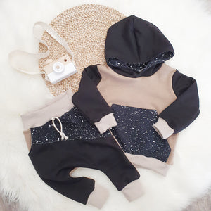 A Lottie & Lysh baby flat lay outfit. Featuring baby sized jogging bottoms in beige and black, with splatter effect accent panel and coordinating hoodie. 