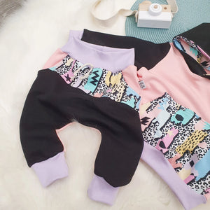 Close up flat lay image of the Lottie & Lysh Yo Mamma harem slouch jogging bottoms for kids. The jogging bottoms are black and pink, and feature a Yo Mama accent panel across the front section. 
