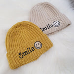 Mustard knitted beanie hat with smile slogan. Cream knitted beanie hat with smiley face embroidery.