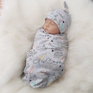 jersey baby swaddle with paper planes print detail. Baby wearing matching knotted hat.