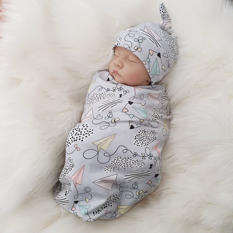 jersey baby swaddle with paper planes print detail. Baby wearing matching knotted hat.