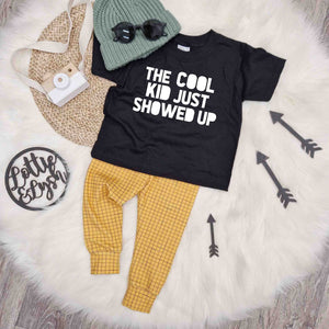 Lottie & Lysh kids outfit inspiration featuring a black t-shirt with 'The Cook Kid Just Showed up Slogan', mustard grid baby and toddler leggings & green knitted beanie hat