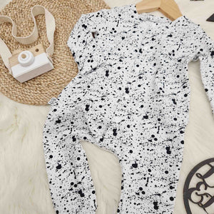 baby outfit flat lay image featuring a white and black babygro with paint splatter effect print