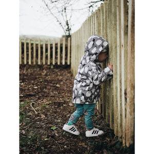 Young toddler wearing lottie and lysh peguin splasher coat and rhino leggings peering through the fence