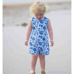 A little girl with blond hair wearing a white and blue floral playsuit 